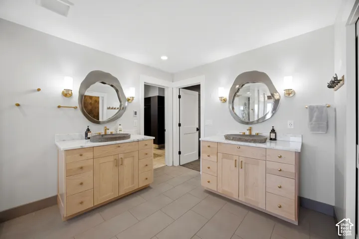 Dual wood-finish vanities with stone vessel sinks, marble countertops, and unique organic-shaped mirrors