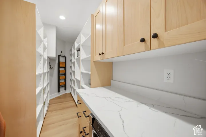 Extensive built-in shelving, wood-finish flooring, light wood cabinetry, white stone-finish countertop, and recessed lighting