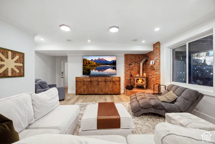 Exposed brick accent wall with a wood-burning stove, recessed lighting, wood-finish flooring, and a large window