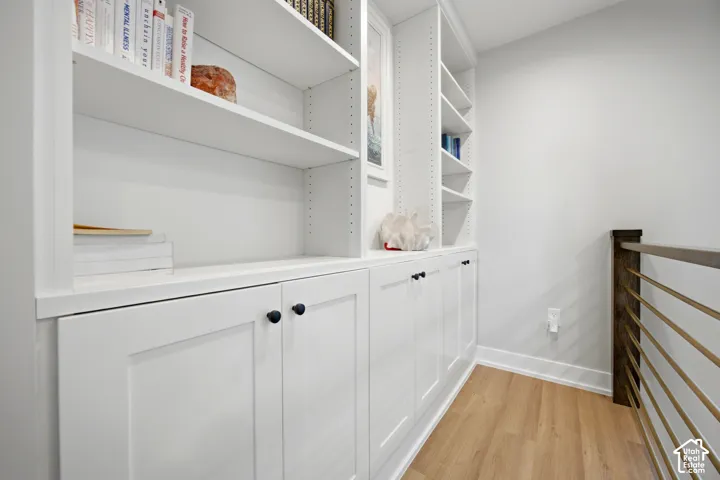 Built-in white cabinetry with black hardware, integrated shelving, wood-finish flooring, and a contemporary metal and wood railing