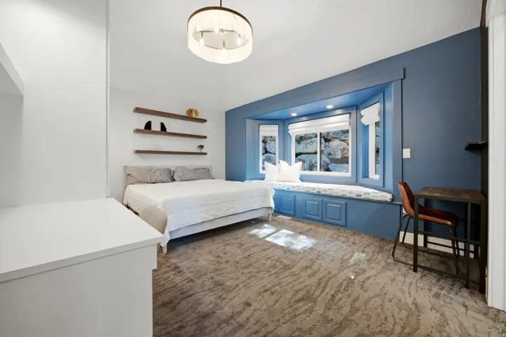Carpeted interior space featuring a built-in window seat with integrated storage, wood-finish floating shelves, and a contemporary ceiling fixture