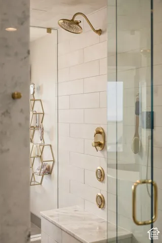 Shower with brass-finish fixtures, white subway tile walls, a built-in marble-finish bench, and a clear glass enclosure