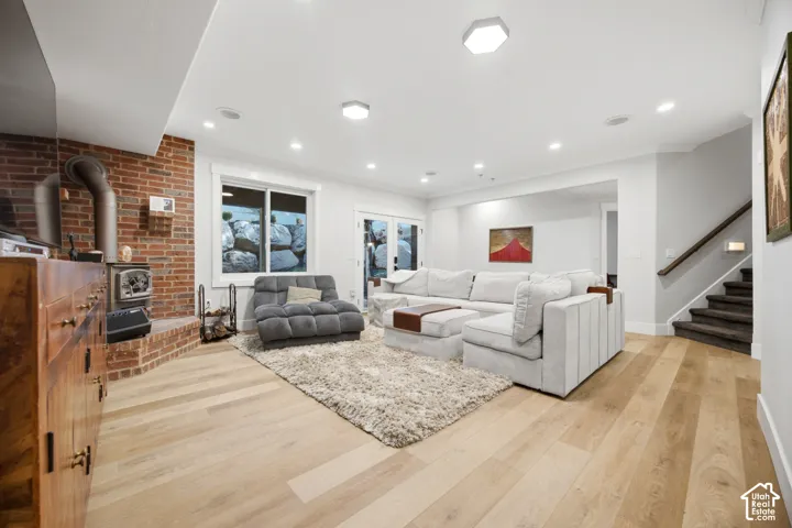 Wood-finish flooring, brick-clad fireplace with a wood stove, recessed lighting, and a staircase with a wood handrail
