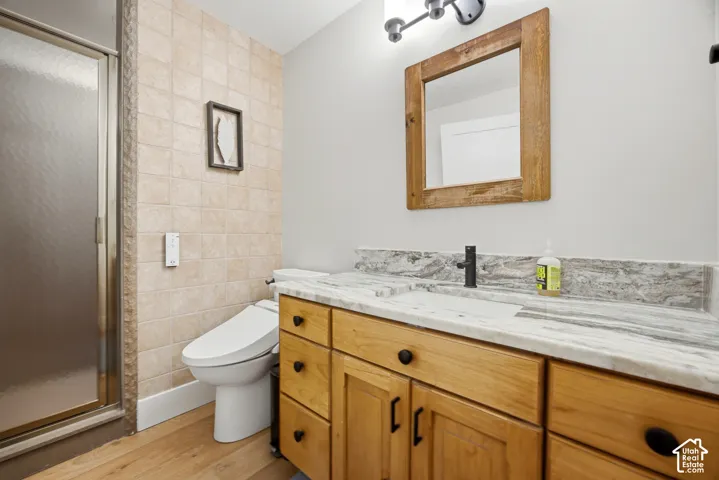 Wood-finish flooring, tiled shower enclosure, natural wood vanity with black hardware, stone countertop, and rustic wood-framed mirror