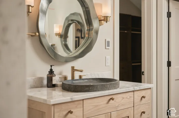 Natural wood vanity with multiple drawers, stone vessel sink, gold-tone faucet, and marble-finish countertop