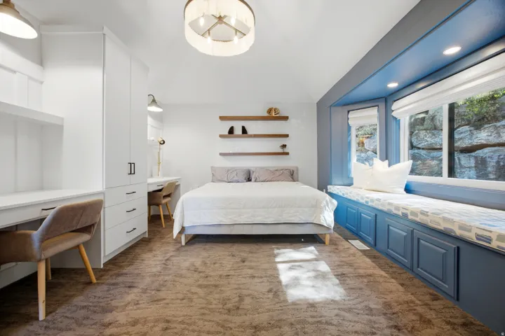 Built-in window seat with integrated storage, custom desks with shelving, recessed lighting, and a vaulted ceiling