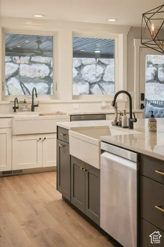 Kitchen featuring wood-finish flooring, two large windows, white and gray cabinetry, a farmhouse sink, and a stainless steel dishwasher