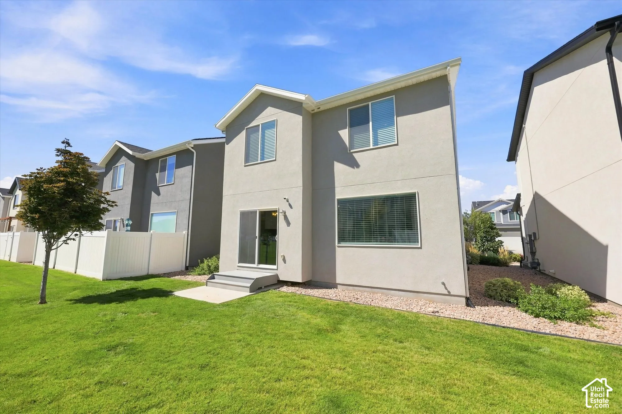 Expansive green lawn with a young tree, white privacy fencing, and a concrete patio