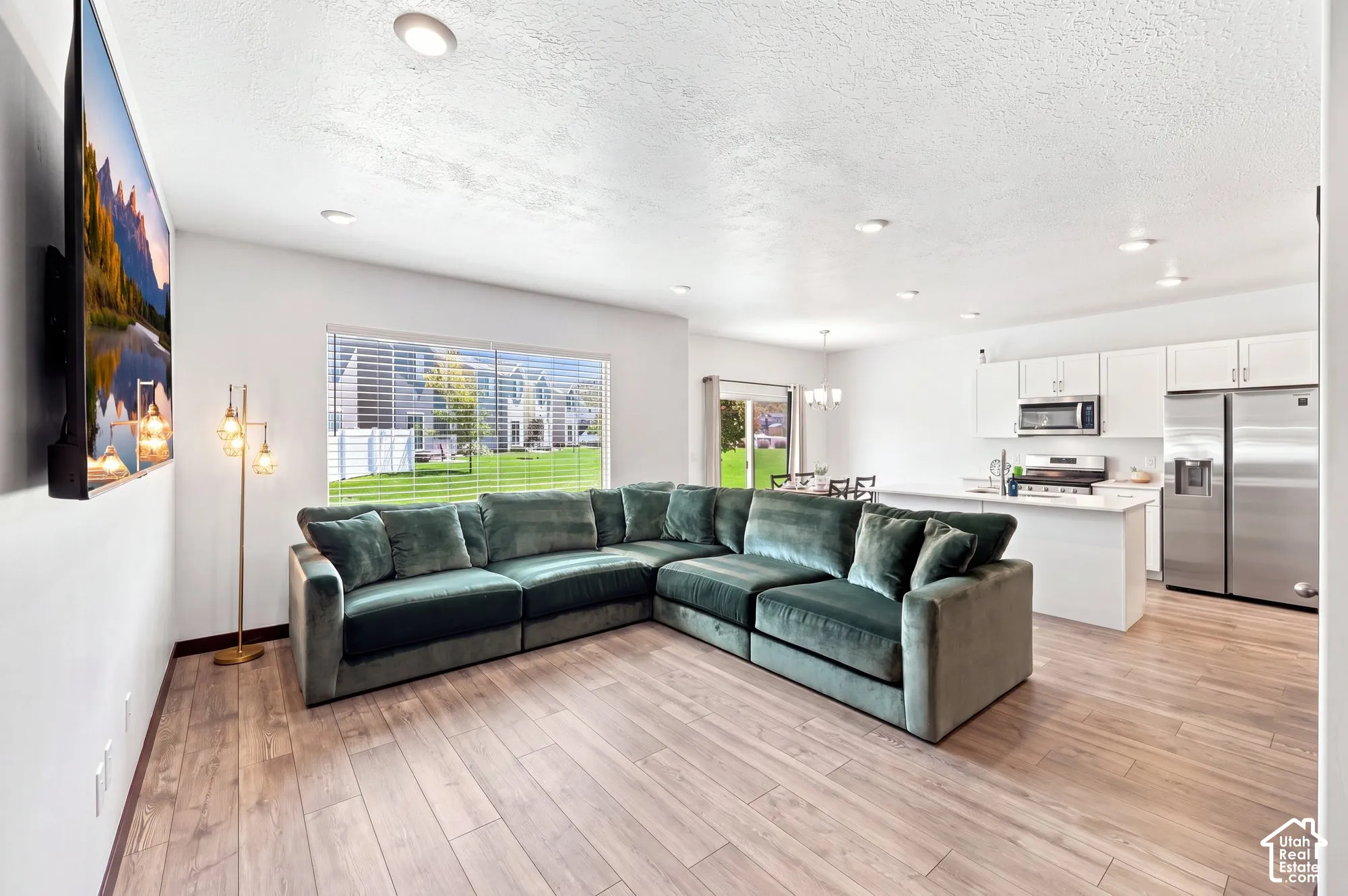 Open-concept living space featuring wood-finish flooring, recessed lighting, and a kitchen with white cabinetry, stainless steel appliances, and a white island "wall color is altered"