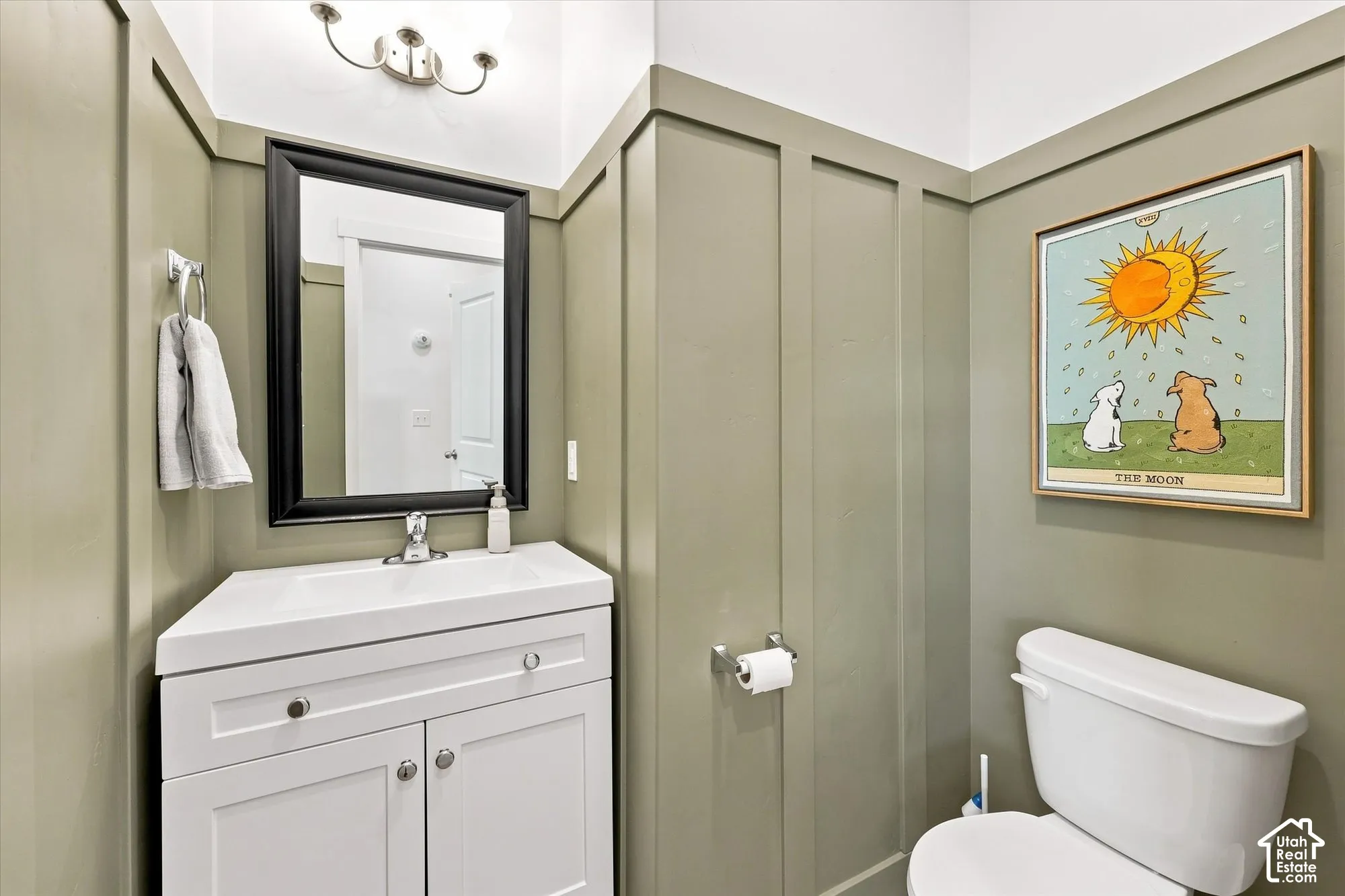 half bath on main floor White vanity with integrated sink, panel molding, and wall-mounted light fixture