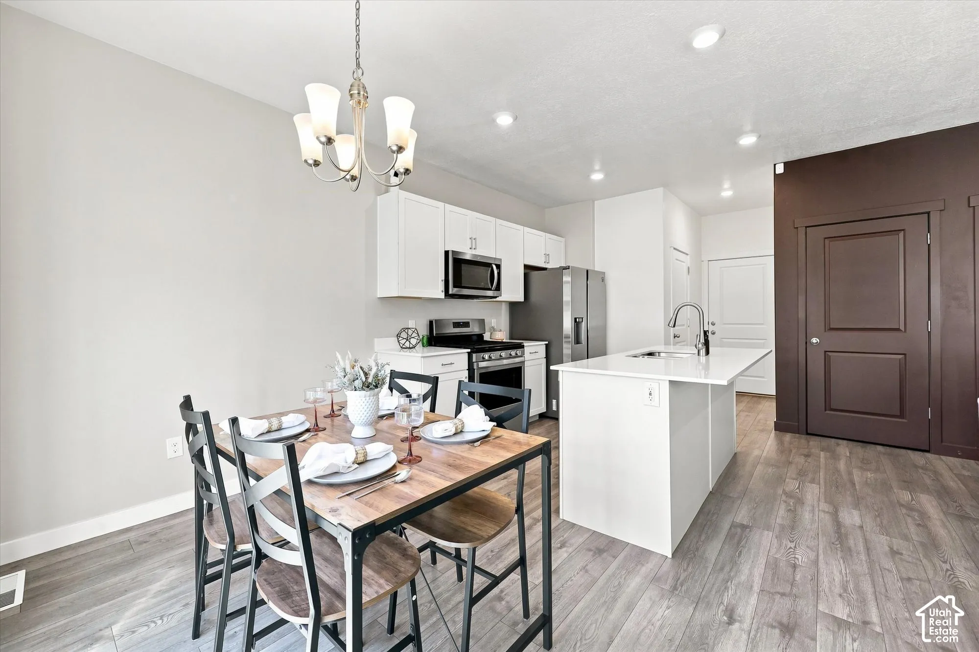 Open-concept kitchen and dining area featuring white cabinetry, stainless steel appliances, a center island with a sink, and wood-finish flooring