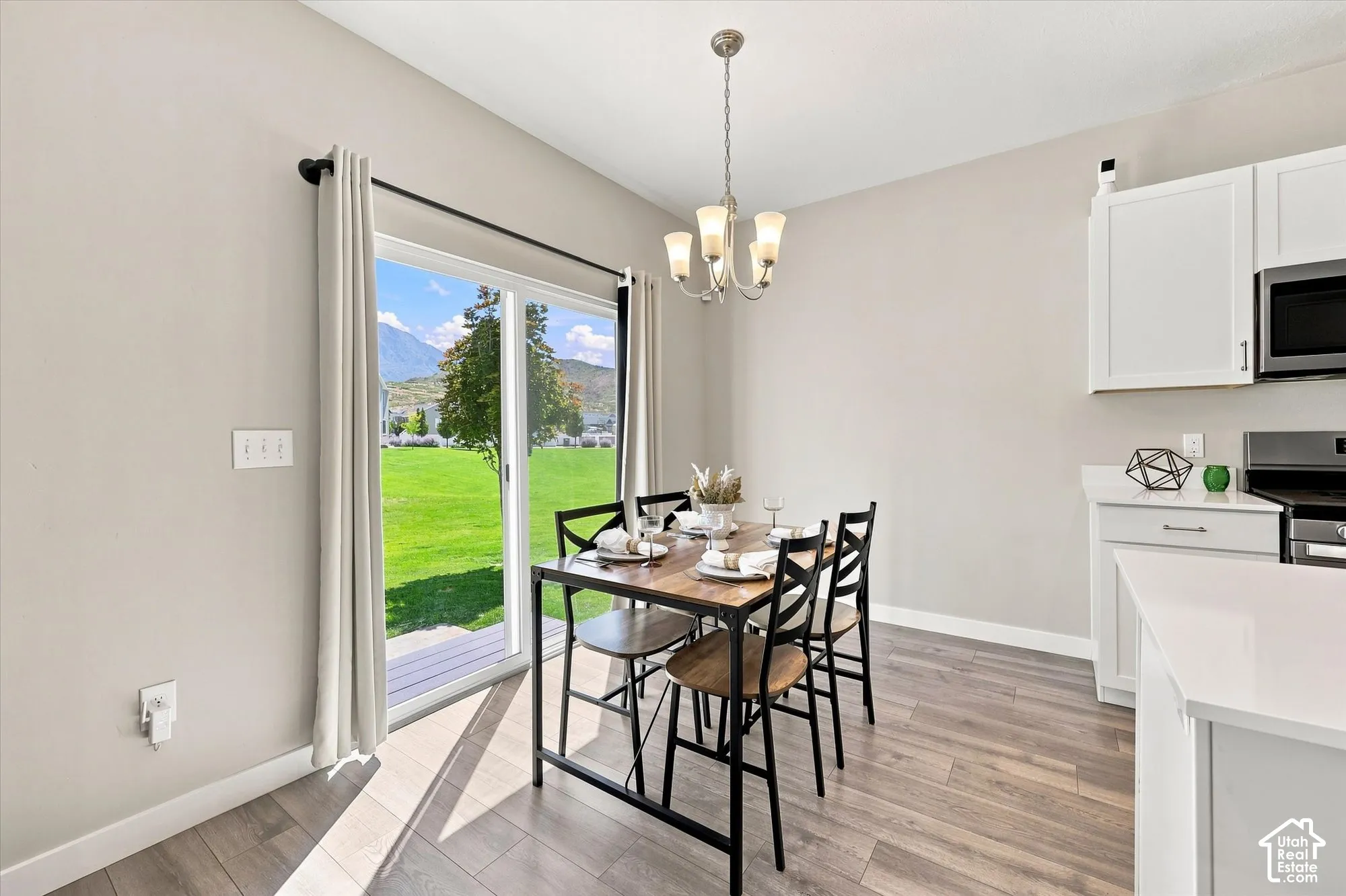 Sliding glass door, wood-finish flooring, white cabinetry, light countertops, and a ceiling-mounted chandelier