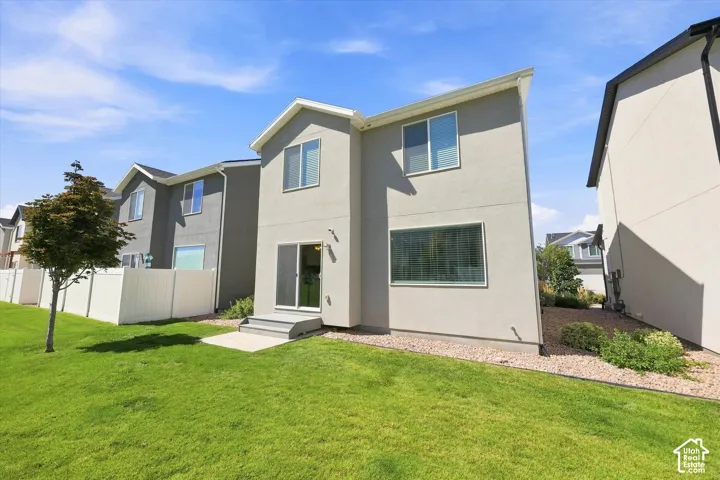 Expansive green lawn with a young tree, white privacy fencing, and a concrete patio