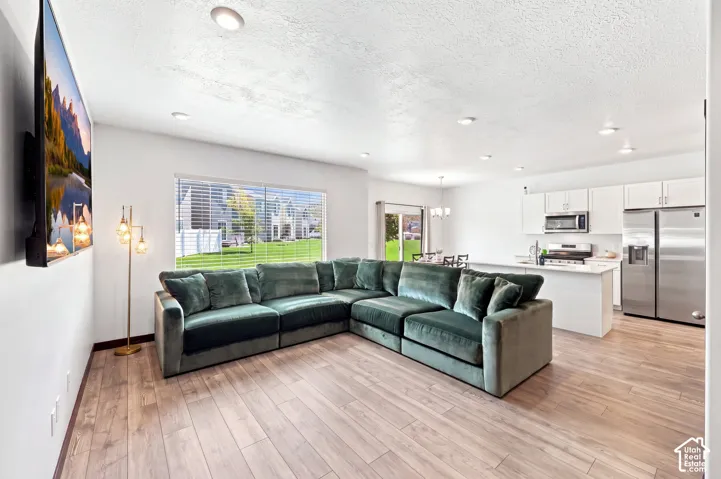 Open-concept living space featuring wood-finish flooring, recessed lighting, and a kitchen with white cabinetry, stainless steel appliances, and a white island "wall color is altered"