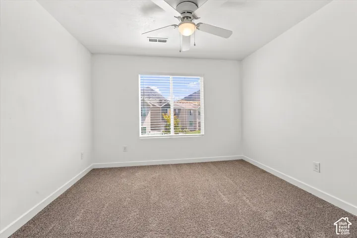 Neutral wall paint, plush carpet flooring, window with blinds, and a ceiling fan with integrated lighting