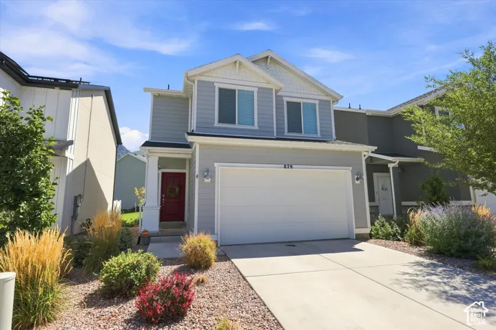 Two-story residence featuring light gray siding, white trim, a covered entry with a red door, a two-car garage, and a concrete driveway