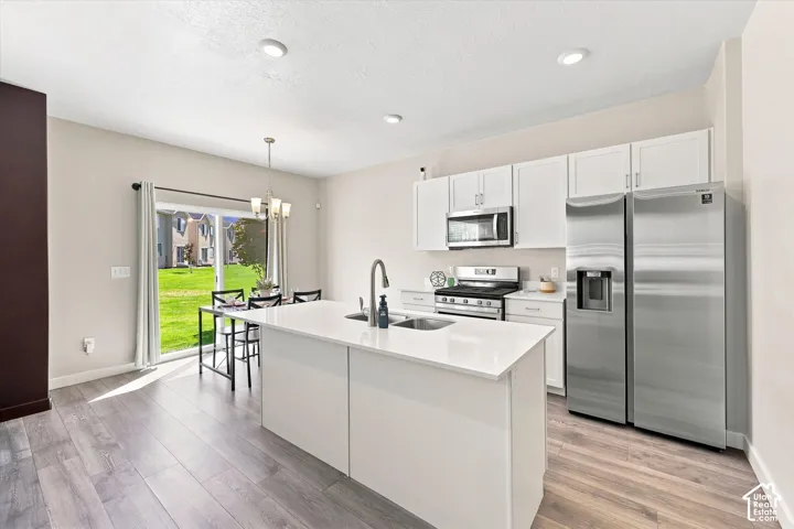 Kitchen featuring white cabinetry, stainless steel appliances, a center island with sink, and wood-finish flooring