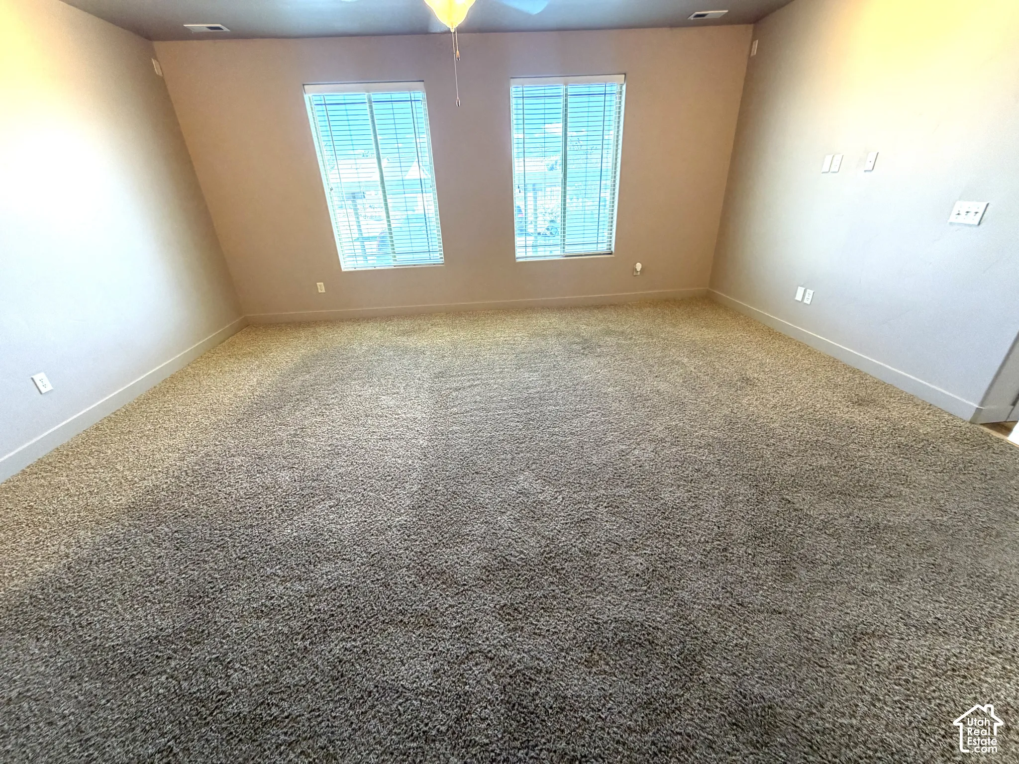 Spacious room with carpet flooring, two windows with blinds, and a ceiling fan