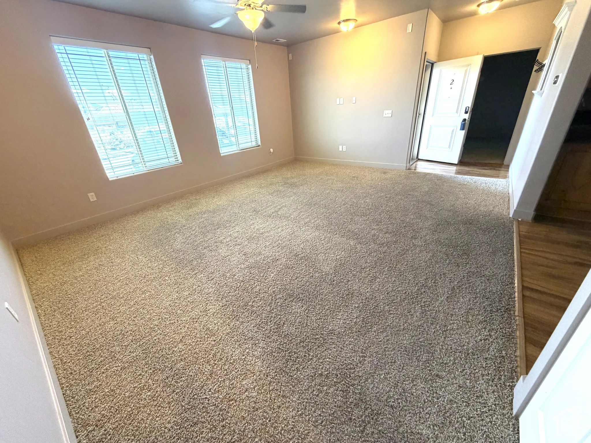 Spacious living area featuring neutral carpeting, high ceilings, multiple windows with blinds, a ceiling fan, and recessed lighting