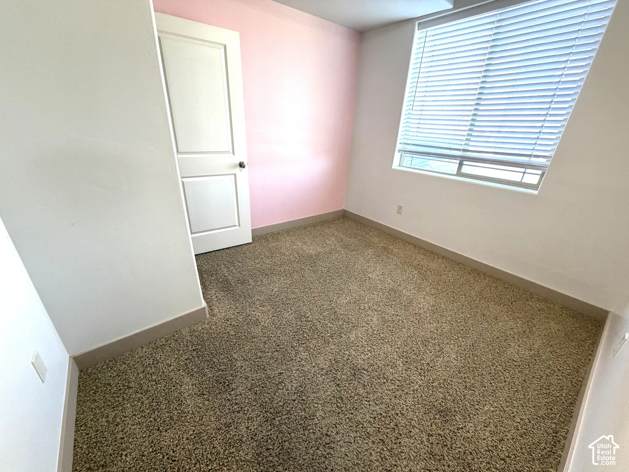Textured carpeting, white interior door, window with horizontal blinds, and two-tone wall finishes