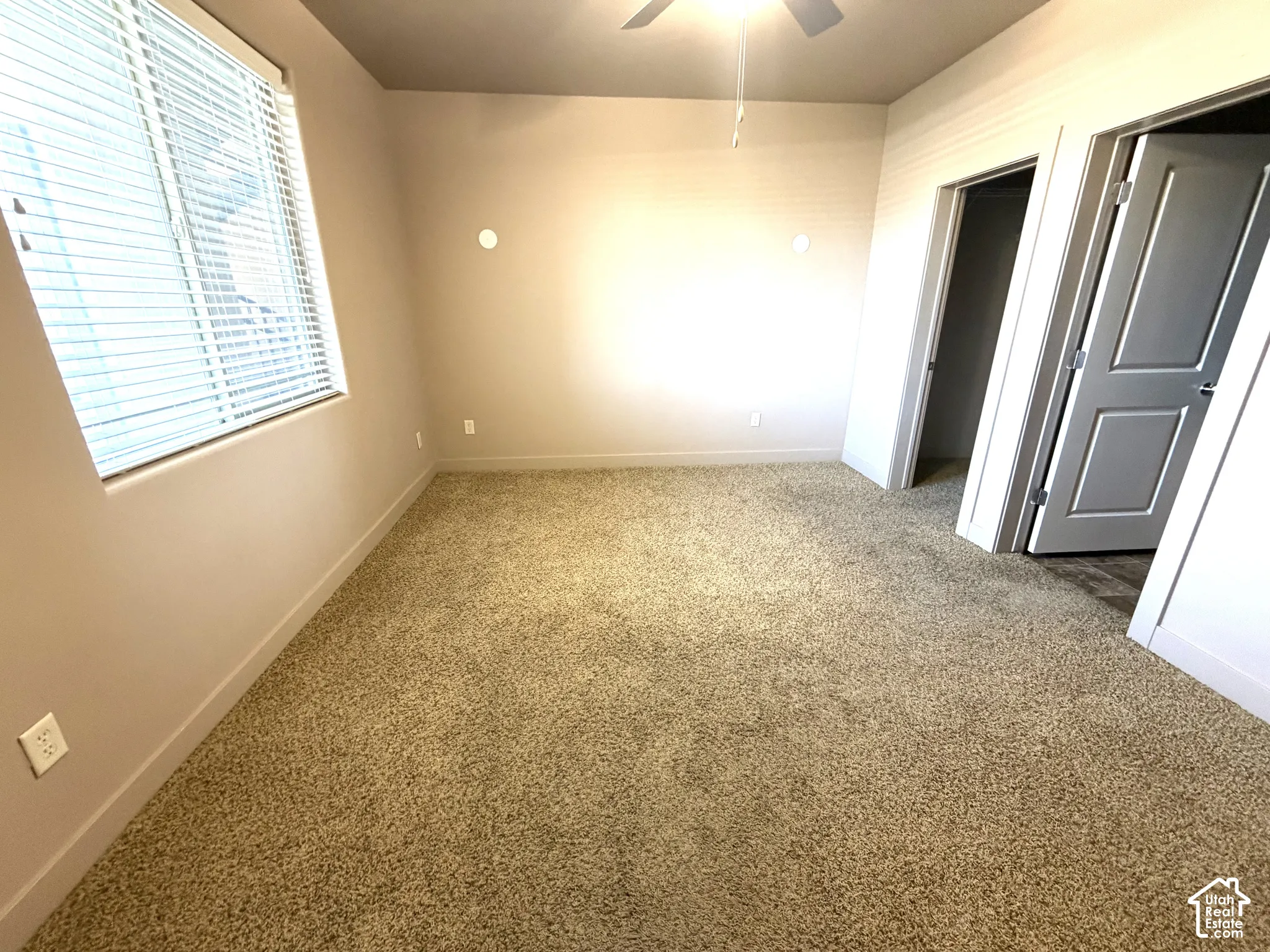 Wall-to-wall carpeting, ceiling fan with integrated lighting, window with blinds, and two panel doors