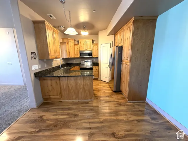 Kitchen featuring wood-finish flooring, natural wood cabinetry, dark stone countertops, and stainless steel appliances