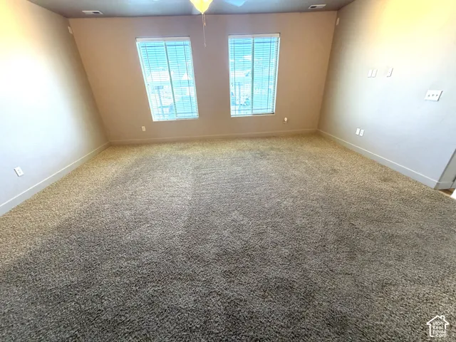 Spacious room with carpet flooring, two windows with blinds, and a ceiling fan