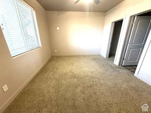 Wall-to-wall carpeting, ceiling fan with integrated lighting, window with blinds, and two panel doors