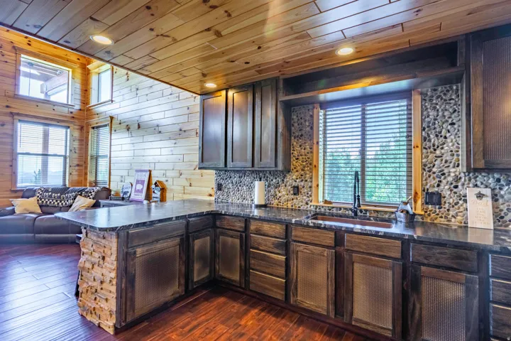 Kitchen featuring wood-finish flooring, dark wood cabinetry, pebble tile backsplash, a window above the sink, and built-in lighting