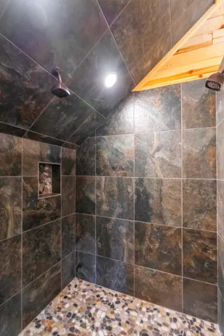 Luxurious walk-in shower featuring large-format slate-look tile walls, a river rock pebble floor, recessed ceiling lighting, and a frameless glass enclosure with polished chrome fixtures