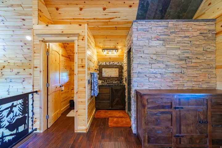 Tongue and groove wood paneling, wood-finish flooring, stone accent wall, vanity with rectangular basin and wood-framed mirror, decorative metal railing