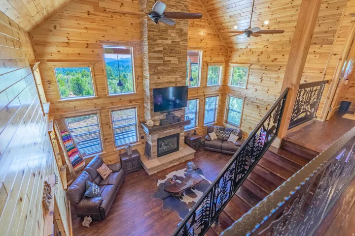 Vaulted wood-paneled ceilings, multi-level windows, stone-clad fireplace with mantel, wood-finish flooring, and decorative metal stair railings