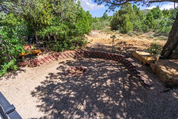 Gravel patio featuring a brick-lined fire pit, natural rock landscaping, and mature trees