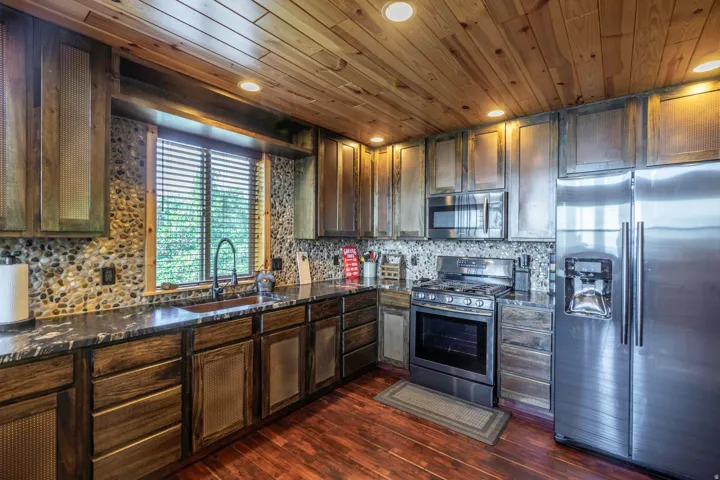 Rustic-inspired kitchen with wood paneling, dark wood-finish cabinetry, stainless steel appliances, and a river rock backsplash