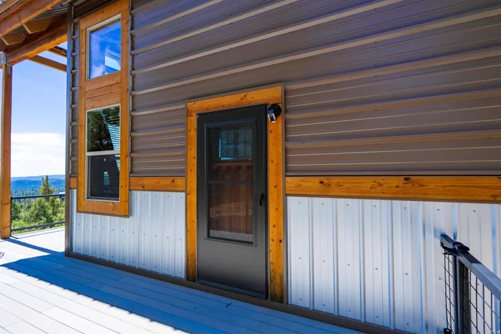 Corrugated metal siding with wood-frame windows and a dark entry door