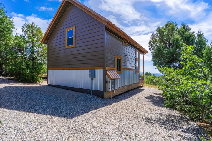 Gable roofline, metal siding exterior, wood-trimmed windows, gravel driveway, and mature landscaping