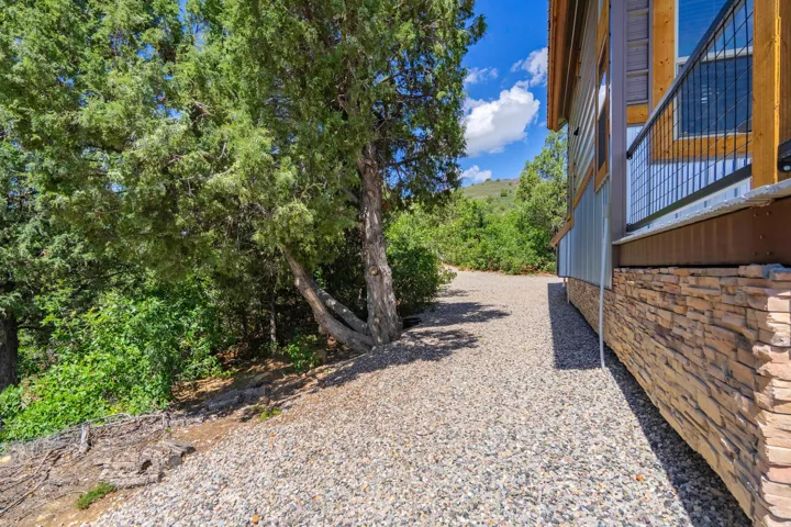 Gravel-finished pathway, stone veneer foundation, corrugated metal siding, and a deck with metal railing
