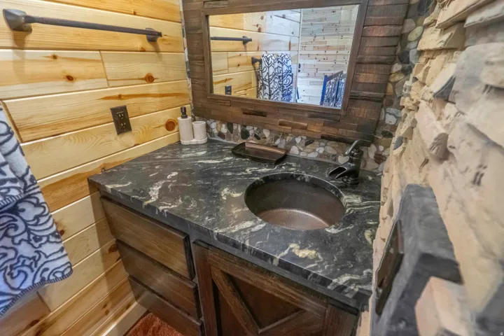 Stone accent wall, wood plank wall finish, dark granite countertop, copper basin sink, and a dark wood vanity