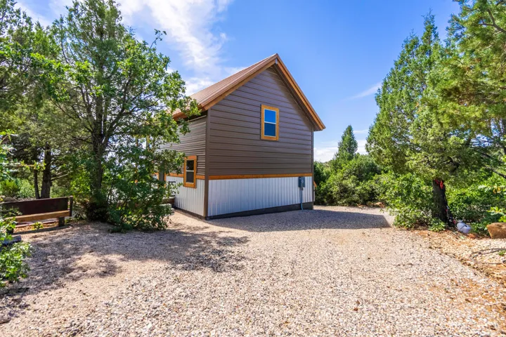 Multi-toned exterior siding with a metal roof and wood-trimmed windows, surrounded by mature trees and a gravel surface