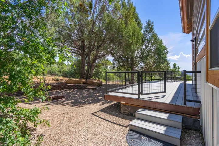 Elevated deck with composite decking and black metal railing, gravel landscaping, built-in tiered stone landscaping, and established trees