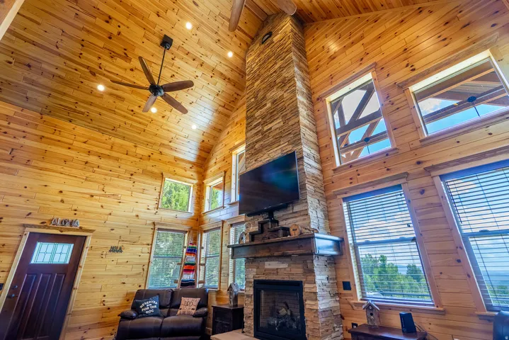 Vaulted wood-paneled ceiling, stone-clad fireplace with wood mantel, recessed lighting, and multiple windows
