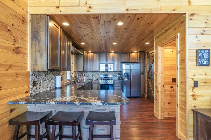Kitchen featuring a stone-clad breakfast bar with a polished countertop, stainless steel appliances, and wood-finish cabinetry