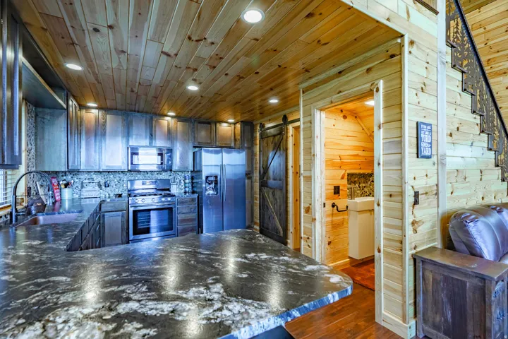 Kitchen featuring wood-finish cabinetry, a patterned backsplash, stainless steel appliances, and a dark stone countertop