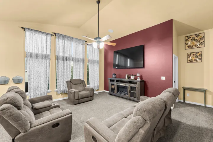 Vaulted ceilings, tall windows with curtain rods, ceiling fan with light fixture, wall-mounted television, and built-in media console with electric fireplace