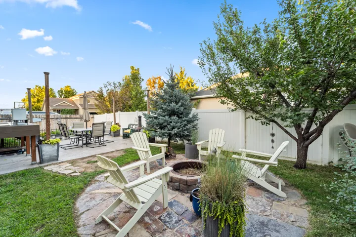 Expansive backyard featuring a stone patio, fire pit, and mature trees