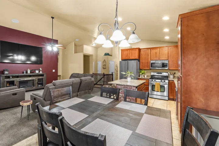 Open-concept living area featuring vaulted ceilings, a kitchen with wood-finish cabinetry, stainless steel appliances, and a stone-clad kitchen island