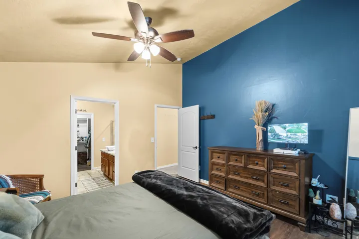 Vaulted ceiling with a ceiling fan, accent wall, and wood-finish flooring
