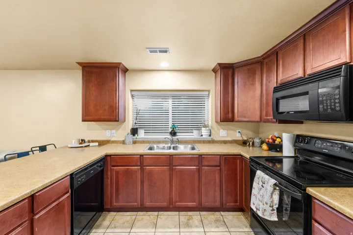 Mother in Law  U-shaped kitchen featuring wood-finish cabinetry, a stainless steel double sink, black appliances, and a breakfast bar