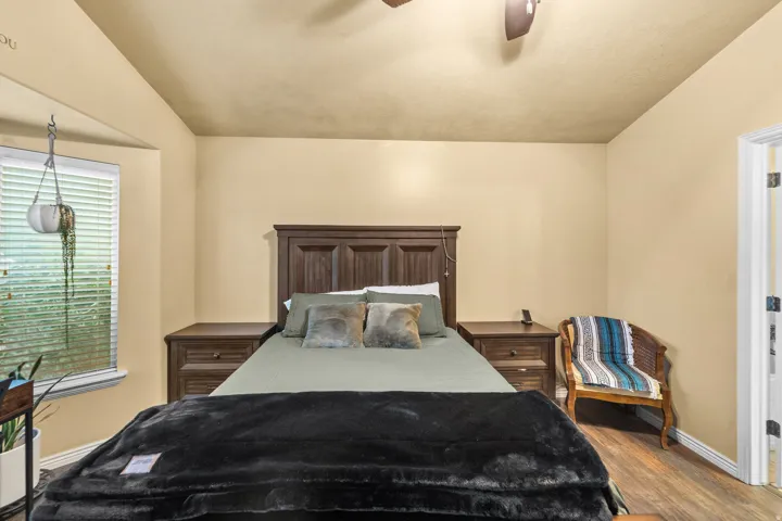 Recessed window with blinds, wood-finish flooring, dark wood-finish bedroom furniture, ceiling fan, and light-toned wall paint