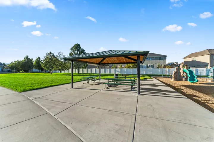 Outdoor recreational area featuring a covered picnic structure, paved pathways, and a children's play structure with a slide